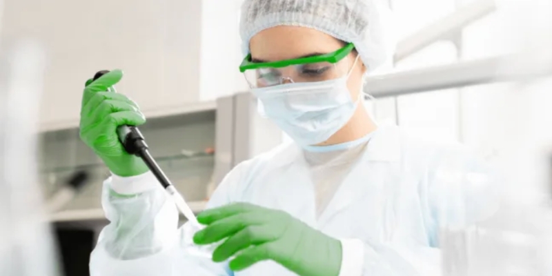 Scientist wearing protective gear and gloves using a pipette in a laboratory